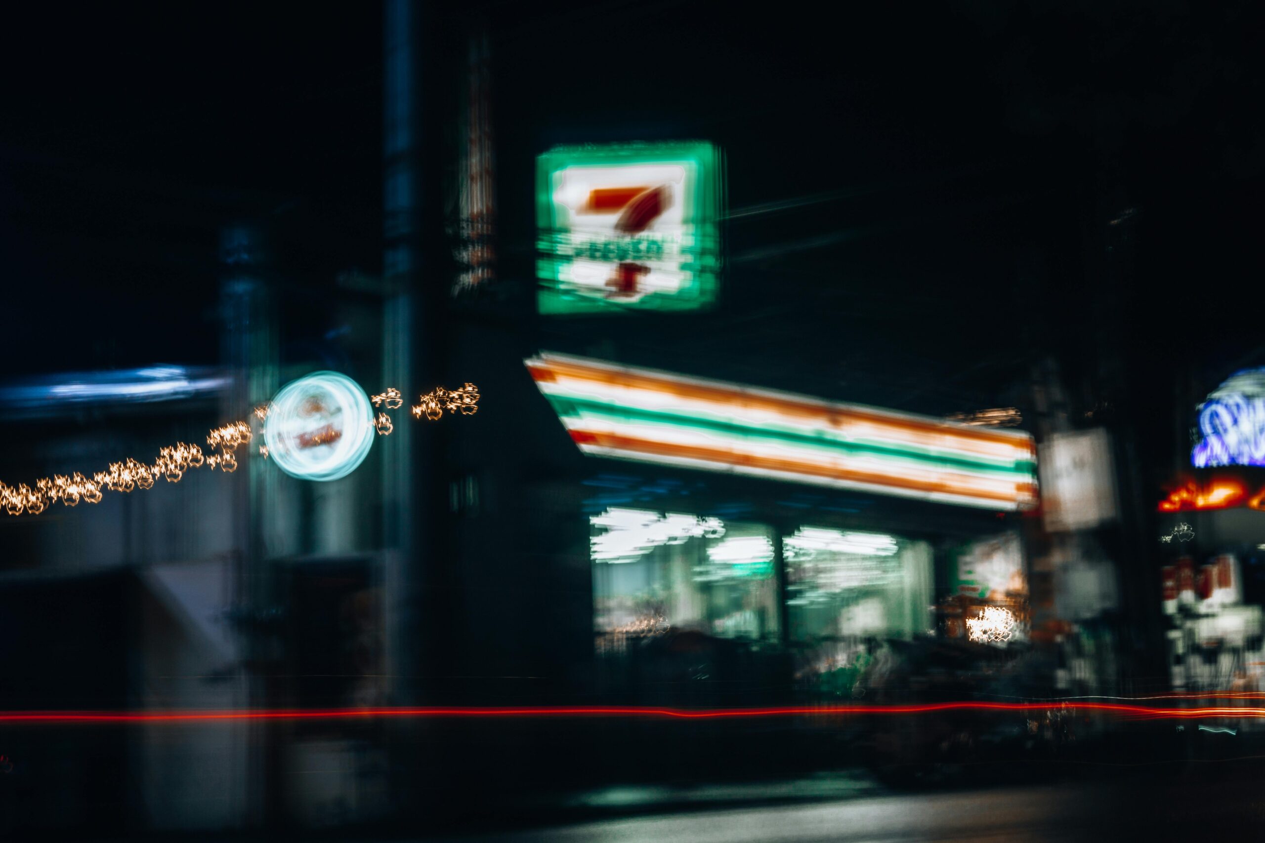 Eine verschwommene Nachtaufnahme einer pulsierenden Stadtszene, die einen geschäftigen Supermarkt mit Neonlichtern zeigt.