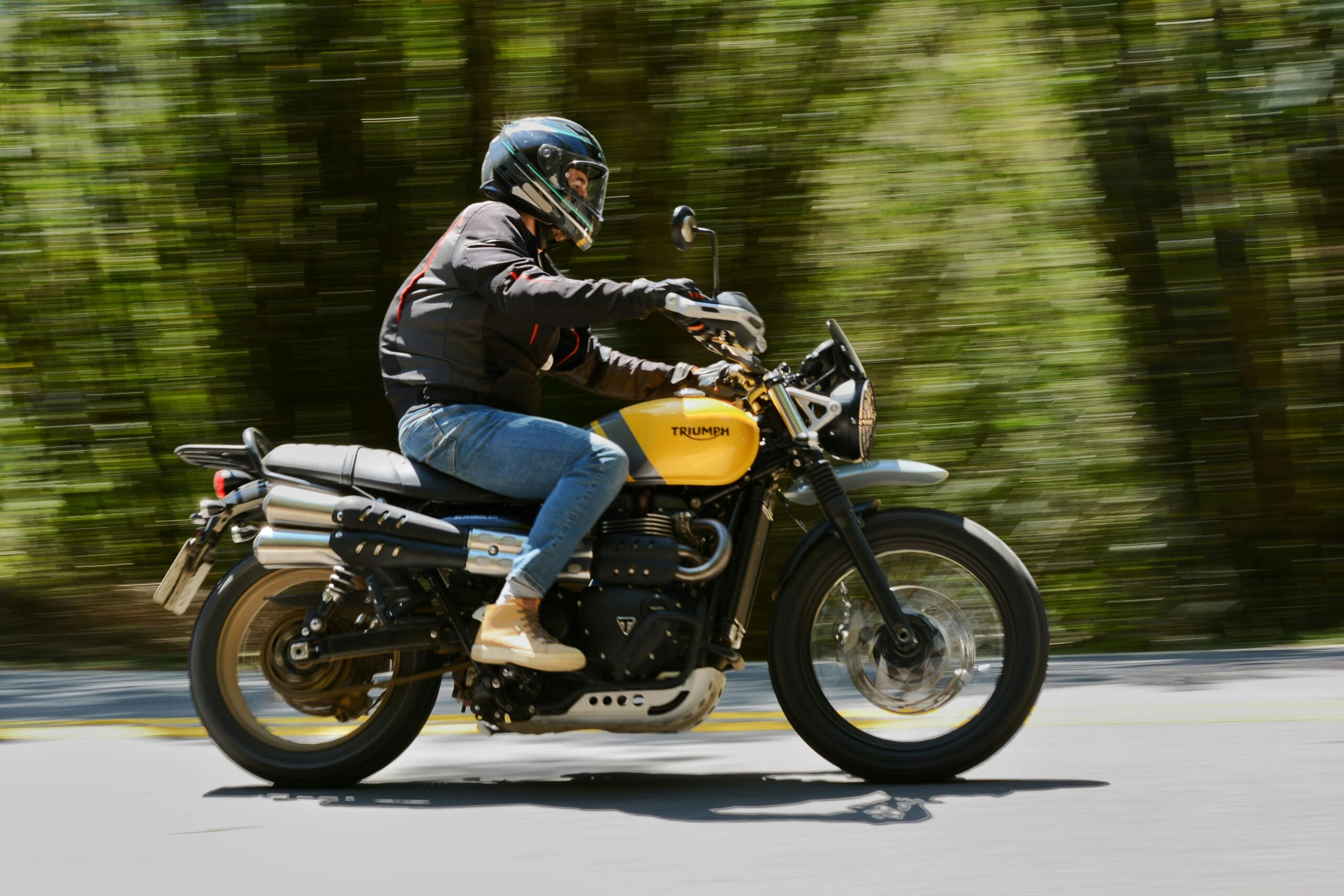 Ein Biker fährt auf einem gelben Triumph-Motorrad durch einen Wald und fängt Bewegung und Geschwindigkeit ein.