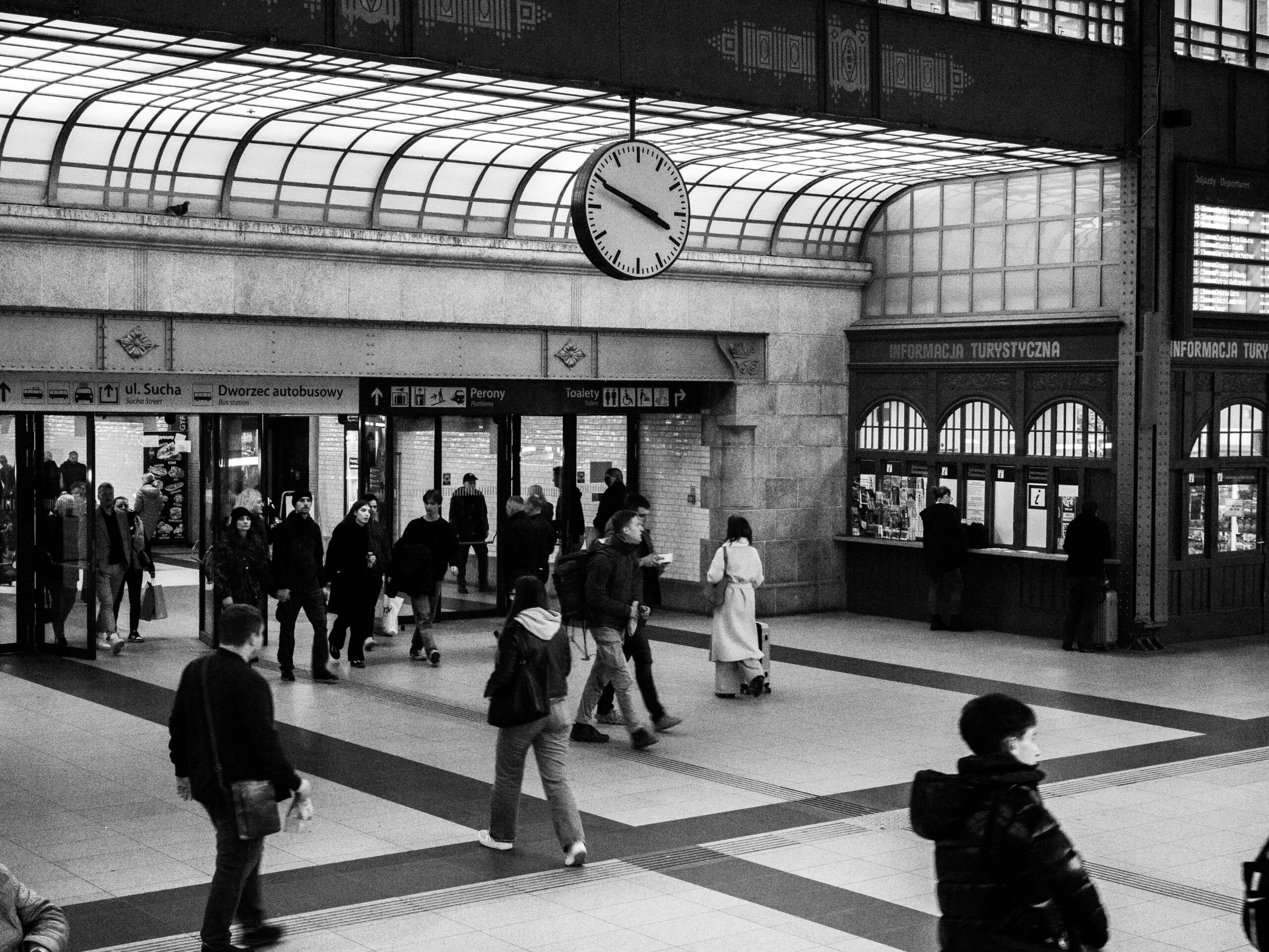 Monochrome Ansicht eines überfüllten Bahnhofs mit einer markanten Uhr und Fahrkartenschaltern.