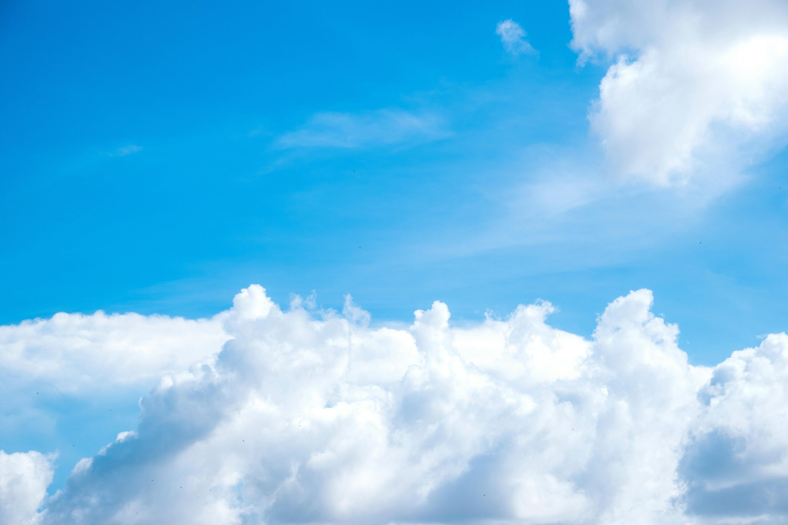 Strahlend blauer Himmel voller flauschiger weißer Wolken an einem klaren Sommertag.