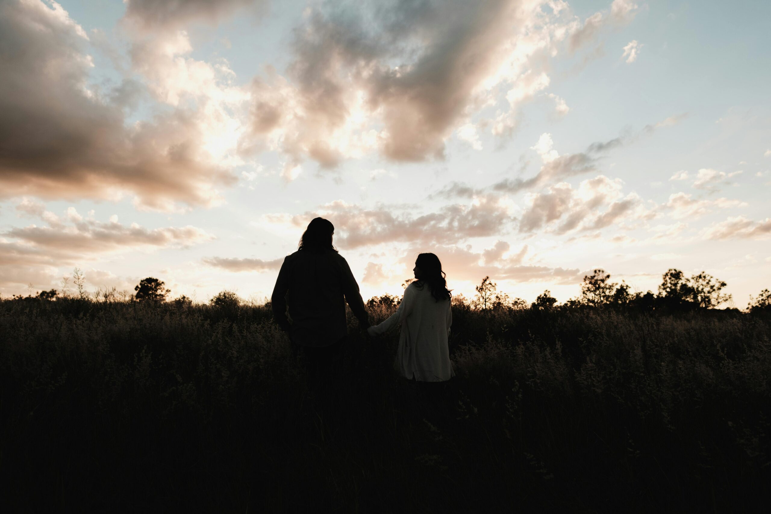 Silhouette eines Paares, das Händchen hält und dabei einen wunderschönen Sonnenuntergang im Freien in einer natürlichen Umgebung beobachtet.