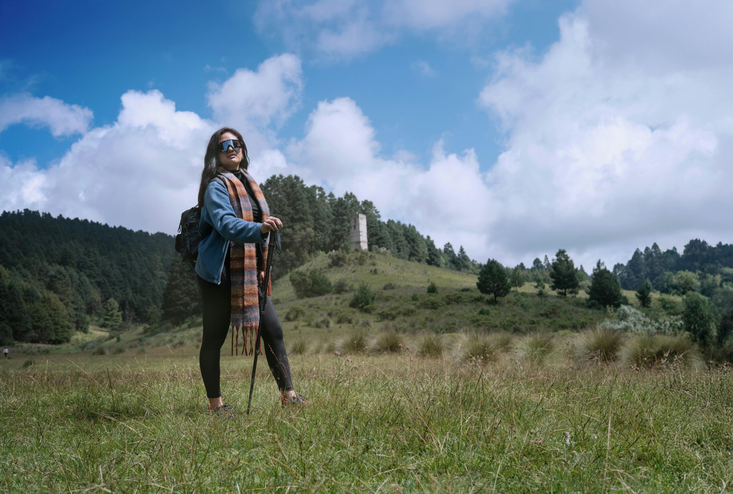 Frau wandert in üppiger Berglandschaft mit blauem Himmel und Wolken.