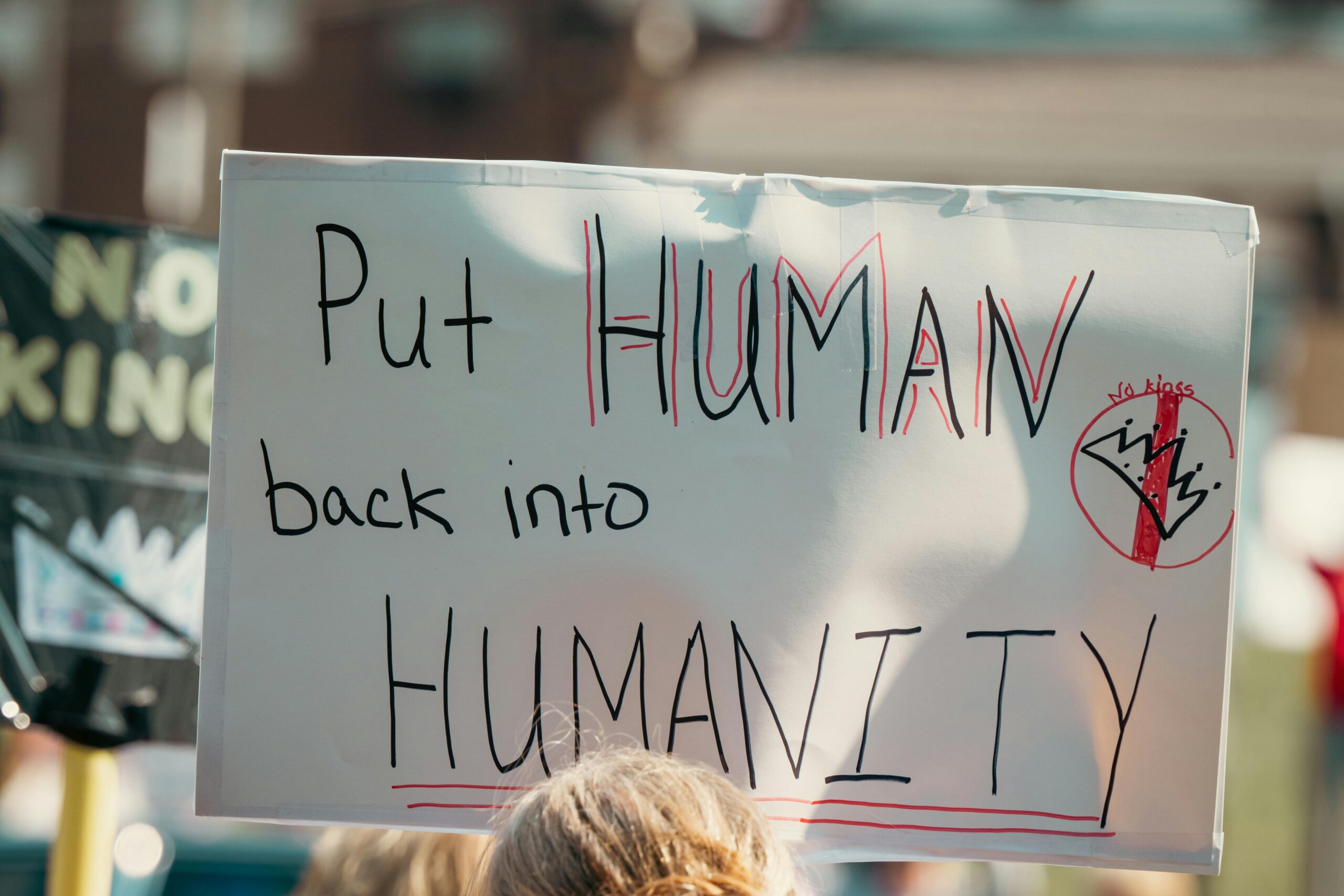 Ein Protestschild mit der Botschaft „Put Human back into Humanity“ während einer Kundgebung bei Tageslicht.