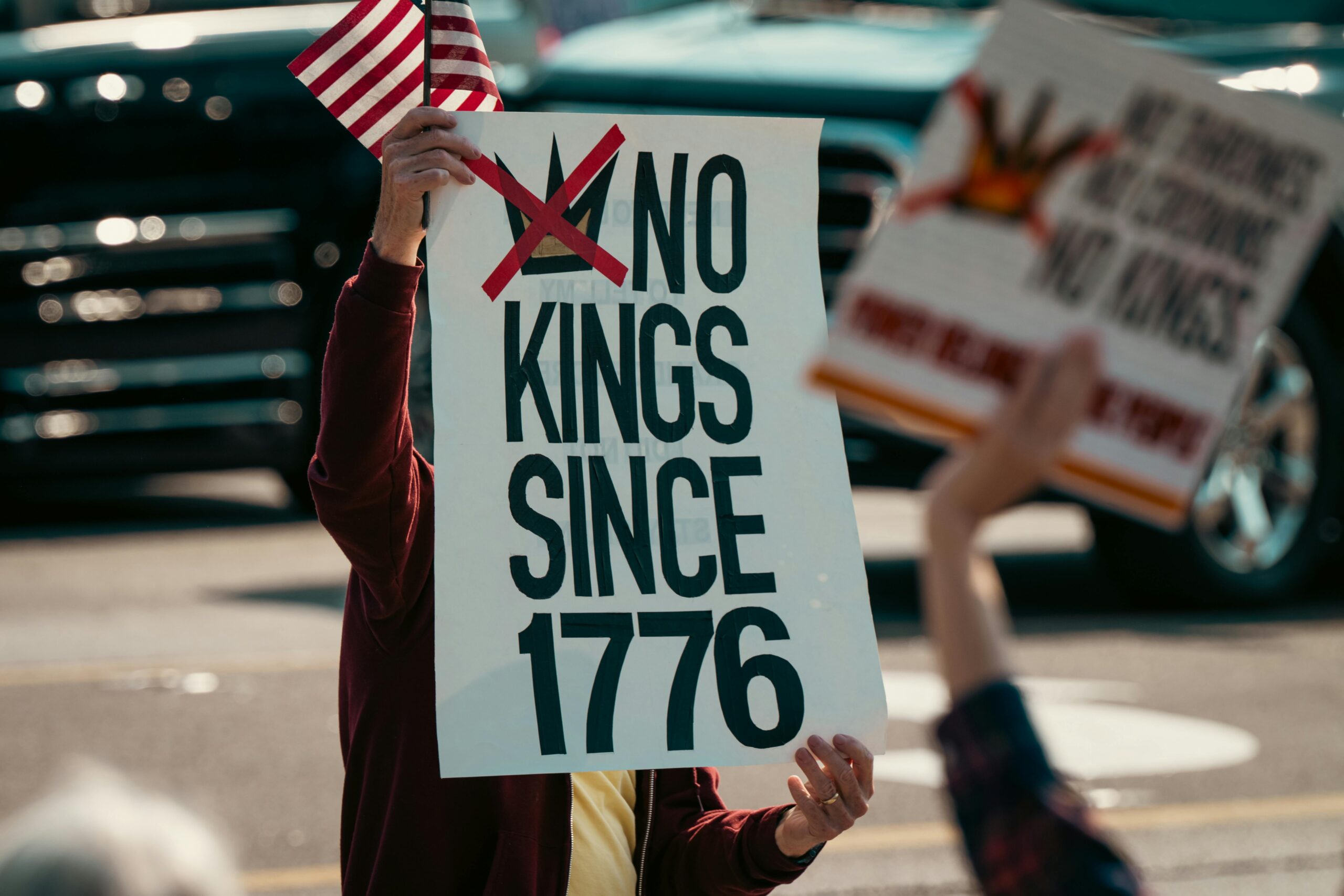Protestschild mit der Aufschrift „Keine Könige seit 1776“, das neben einer kleinen US-Flagge gehalten wird und demokratische Gefühle betont.