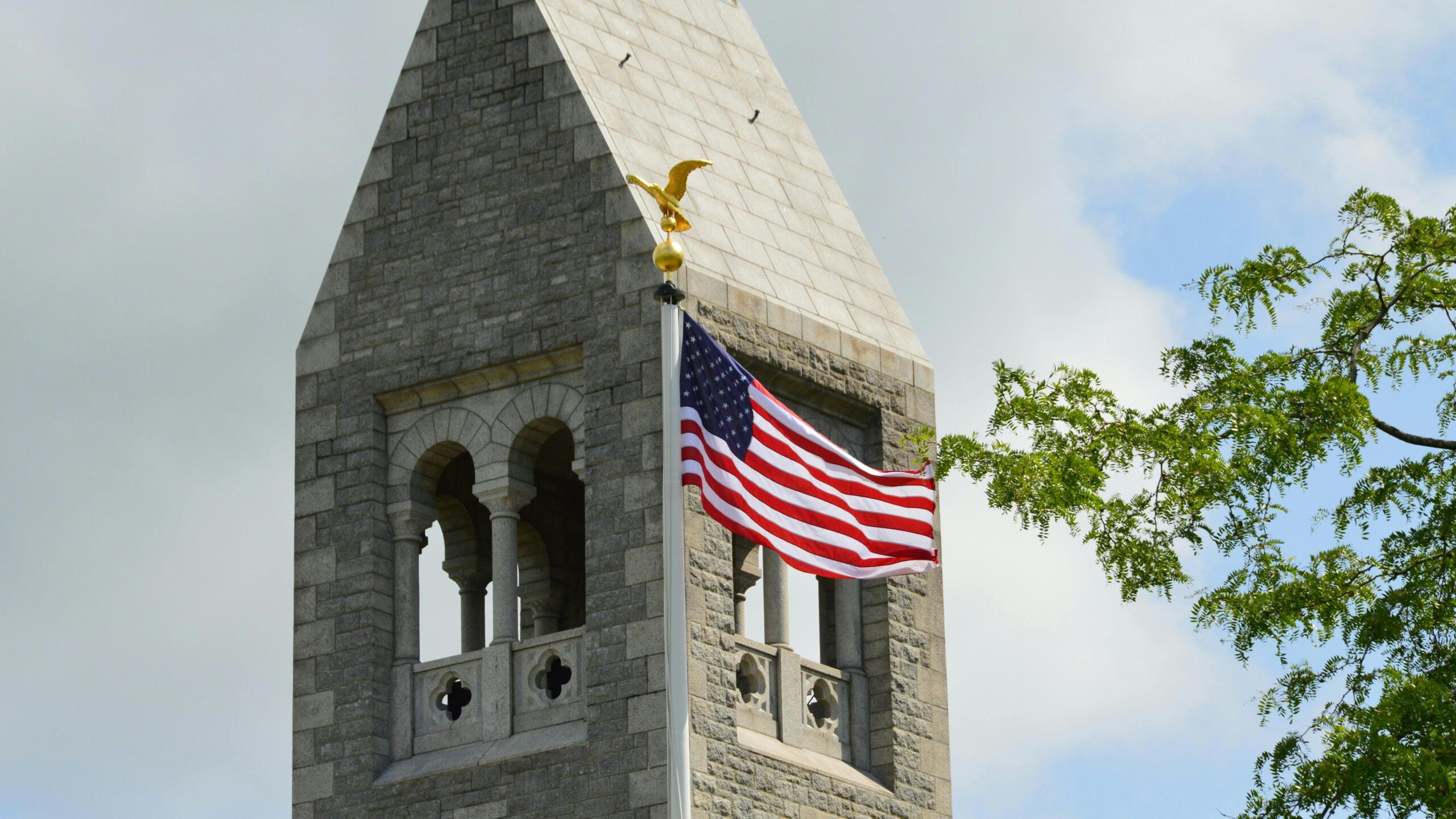 Ein historischer steinerner Glockenturm mit einer wehenden amerikanischen Flagge vor einem blauen Himmel in der Normandie, Frankreich.