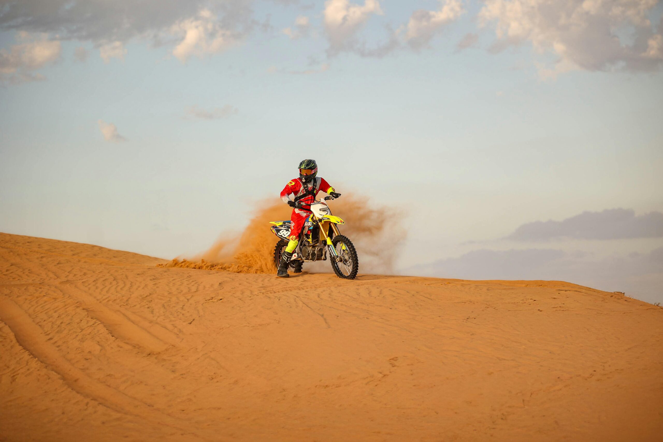 Ein Motorradfahrer in auffälliger Montur rast über die Wüstendünen und hinterlässt eine Sandspur.