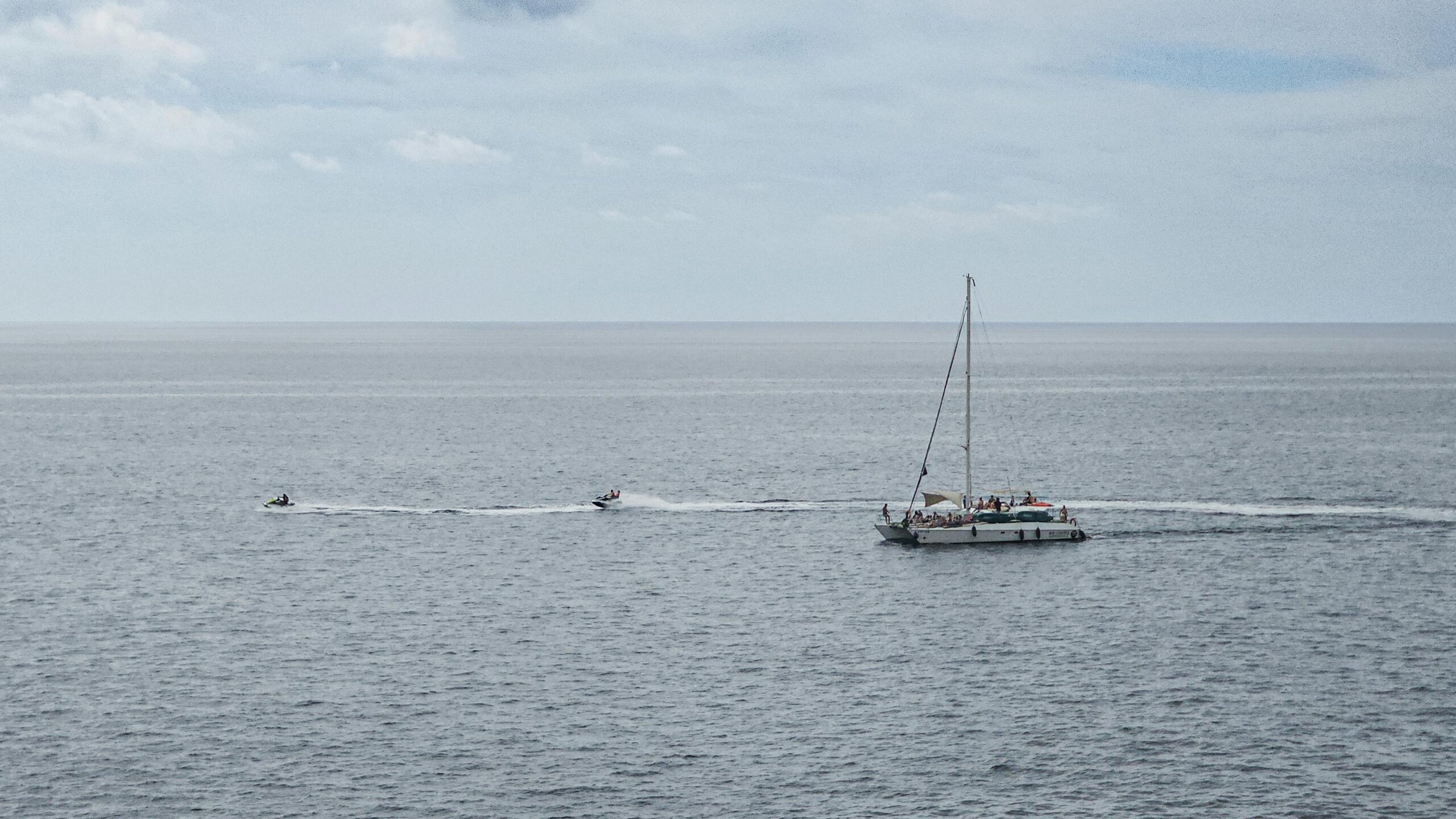 Ein malerischer Blick auf ein Segelboot und Jetskis auf einem riesigen Ozean bei Tag.